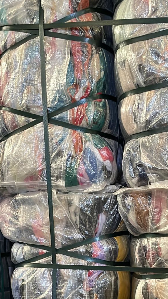 Pallets de vêtements emballés dans des sacs plastiques transparents, reliés par des sangles vertes, prêts au stockage. - Wholesale budget from FRIPEIN STORE UNITED, France